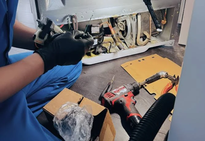 Gloved technician examining appliance components with repair tools nearby