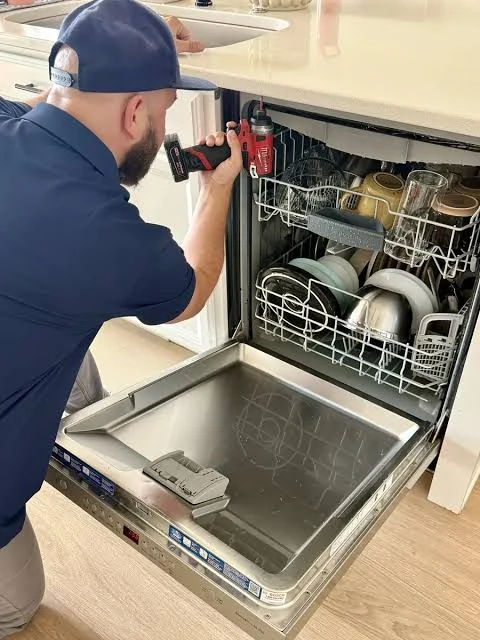 Technician using a drill while inspecting an open dishwasher